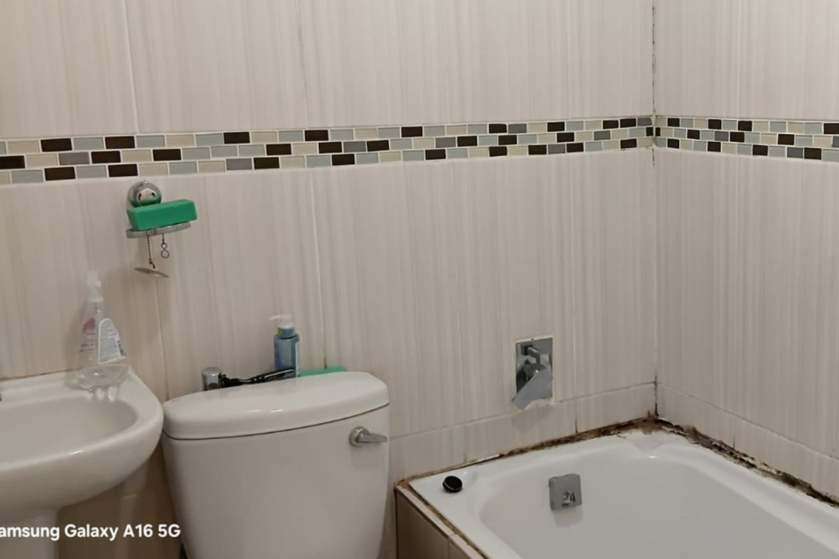 Compact bathroom featuring a white toilet, wall-mounted basin, and a bathtub with tiled walls and a decorative mosaic border.