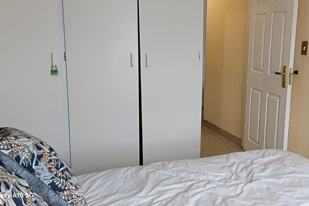 A bedroom featuring built-in white cupboards and a standard interior door, leading into a tiled hallway area.