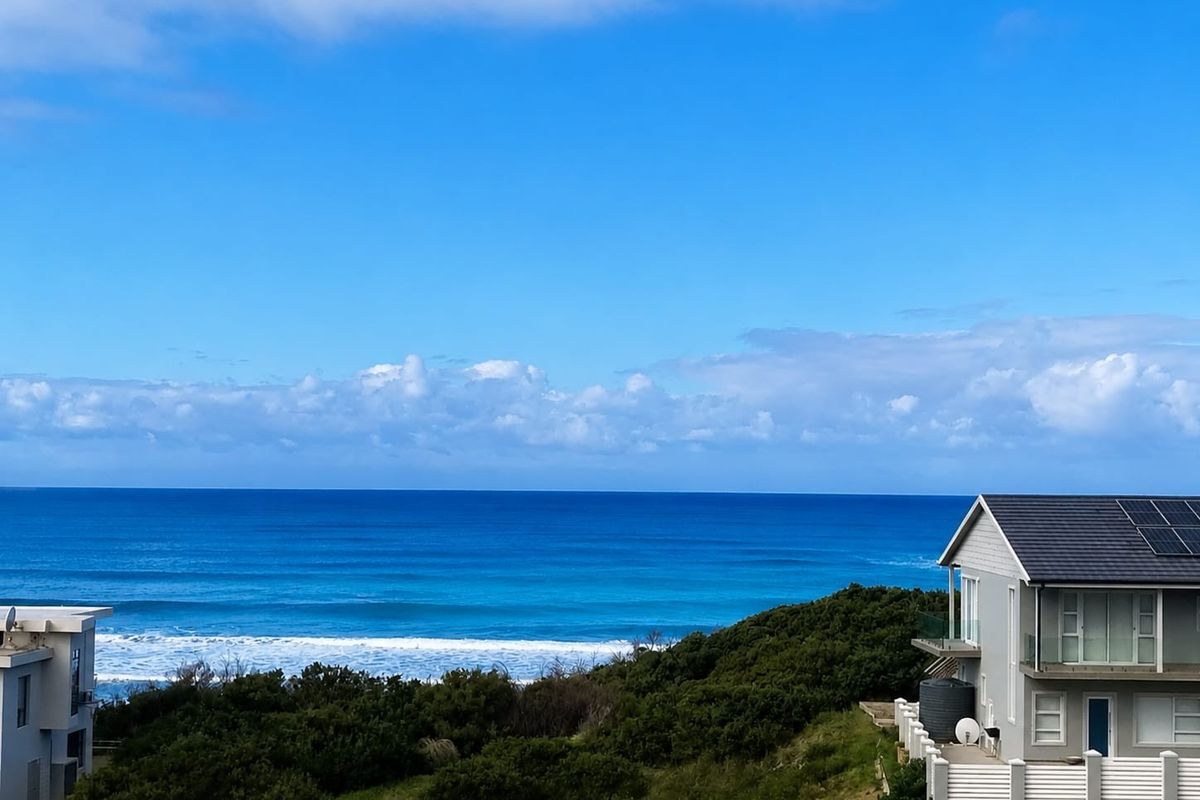 A scenic elevated view of the ocean coastline featuring nearby residential properties with solar panels and coastal vegetation.