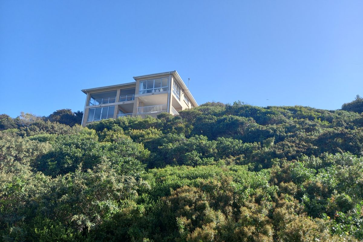 An elevated residential property situated on a hillside, featuring large windows and balconies overlooking the surrounding natural landscape.