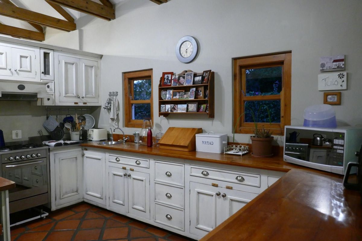 A rustic-style kitchen featuring white cabinetry, wooden countertops, terracotta floor tiles, and exposed timber ceiling beams.