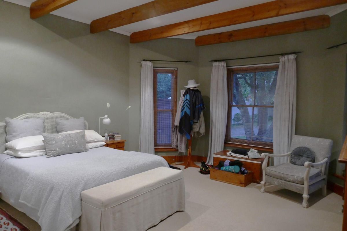 Spacious bedroom featuring exposed timber ceiling beams, sash windows with wooden frames, and neutral carpeting.