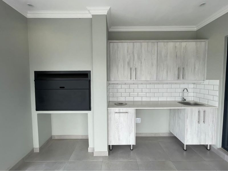 A modern outdoor entertainment area featuring a built-in braai, stone-look cabinetry, subway tile backsplash, and a stainless steel prep sink.