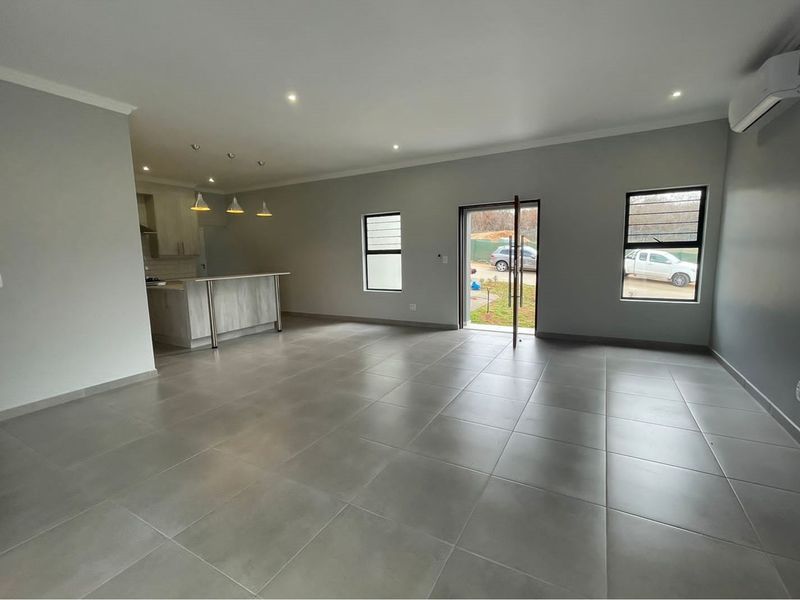 Spacious open-plan living area featuring large format floor tiles, recessed downlighting, and a modern kitchen with a breakfast bar and pendant lighting.