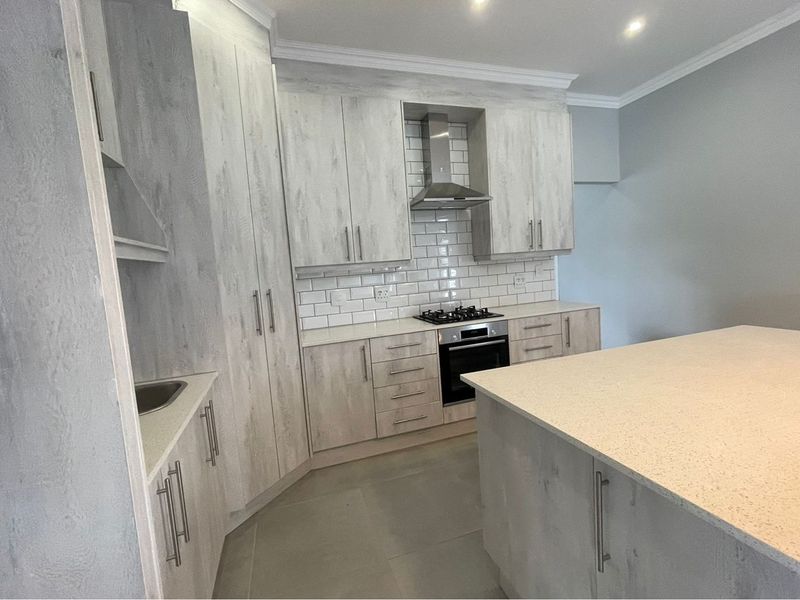 Modern kitchen featuring light wood-grain cabinetry, stone countertops, a central island, built-in oven, gas hob, and a classic subway tile backsplash.