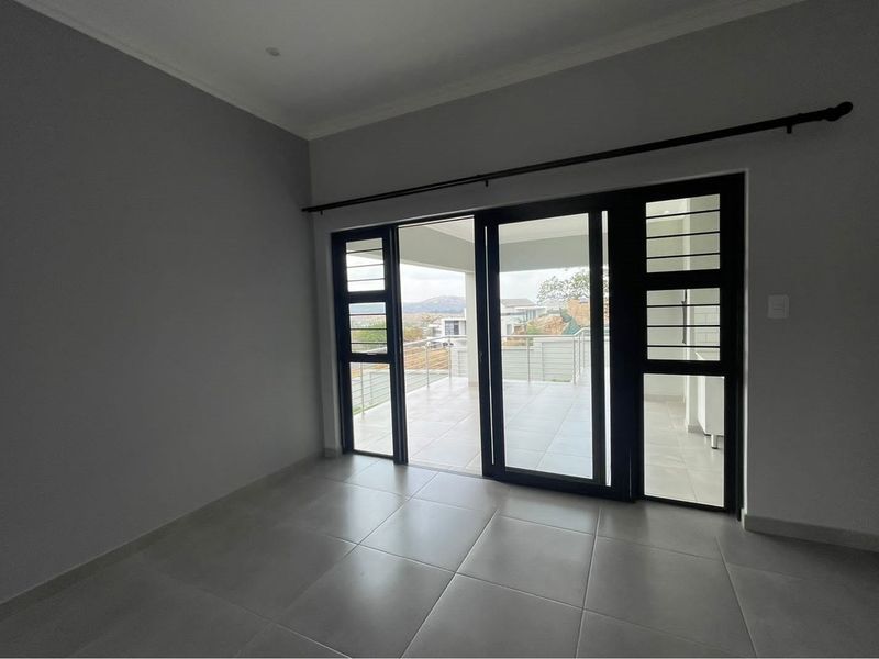 An empty living area featuring large black-framed sliding glass doors that open onto a tiled patio with scenic views.
