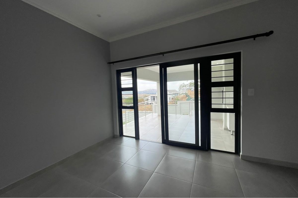 An empty living area featuring large black-framed sliding glass doors that open onto a tiled patio with scenic views.