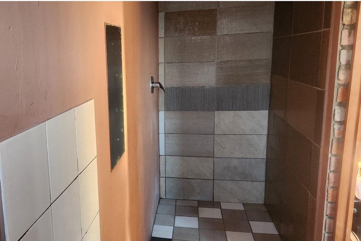 A shower area featuring a mix of tiled wall finishes, exposed brickwork, and a wall-mounted shower fixture.