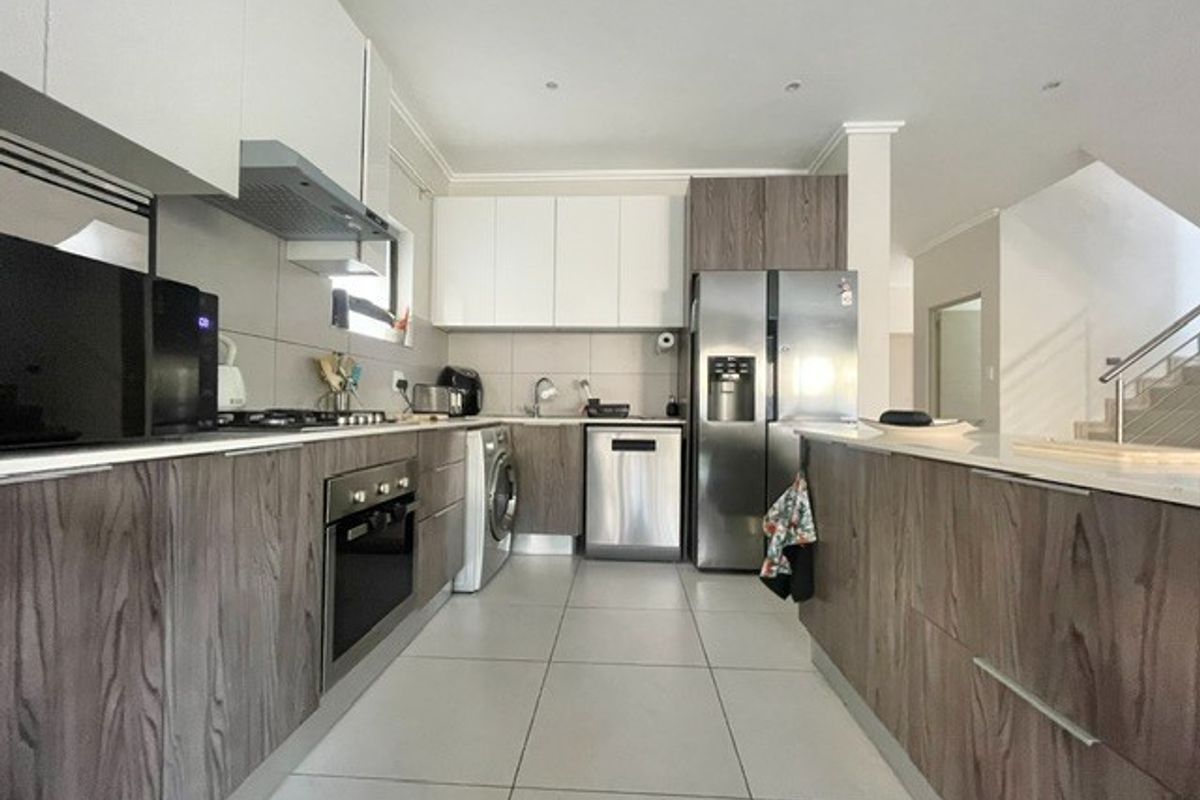 Modern kitchen featuring wood-grain and white cabinetry, stone countertops, integrated appliances, and tiled flooring, offering a clean and functional workspace.