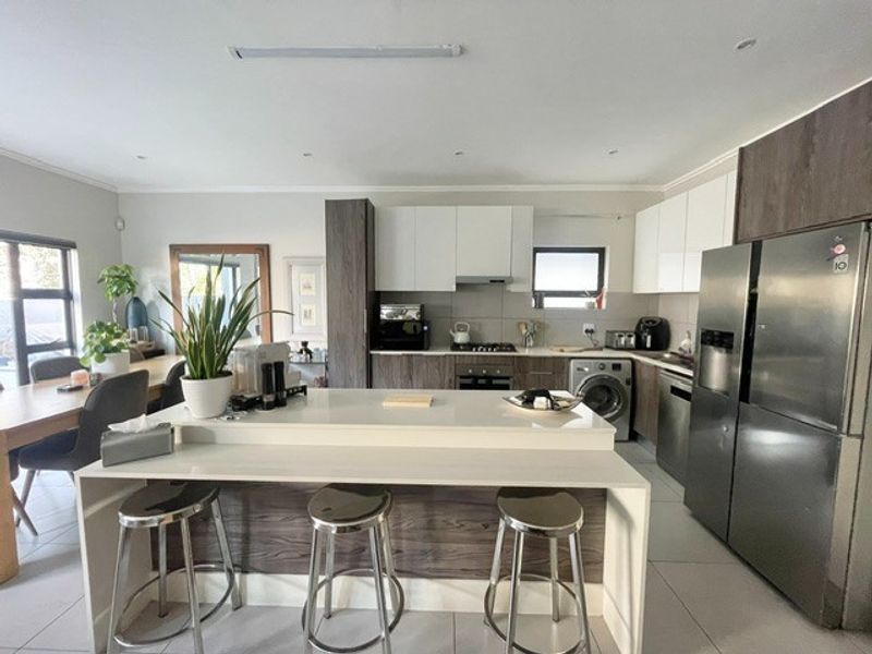 Modern open-plan kitchen featuring a central island, sleek two-tone cabinetry, stone countertops, and integrated appliances, seamlessly flowing into the dining area.