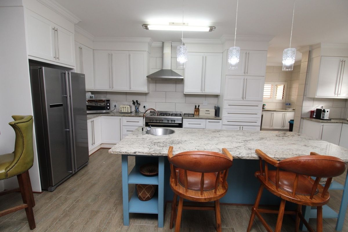 Modern kitchen featuring white cabinetry, granite countertops, a central island with a prep sink, and stainless steel appliances including a gas range and extractor fan.