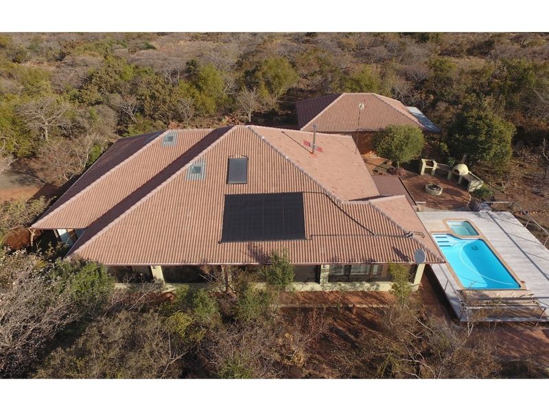 Aerial view of the property featuring a tiled roof with solar panels, a swimming pool, and an outdoor entertainment area with a built-in braai.