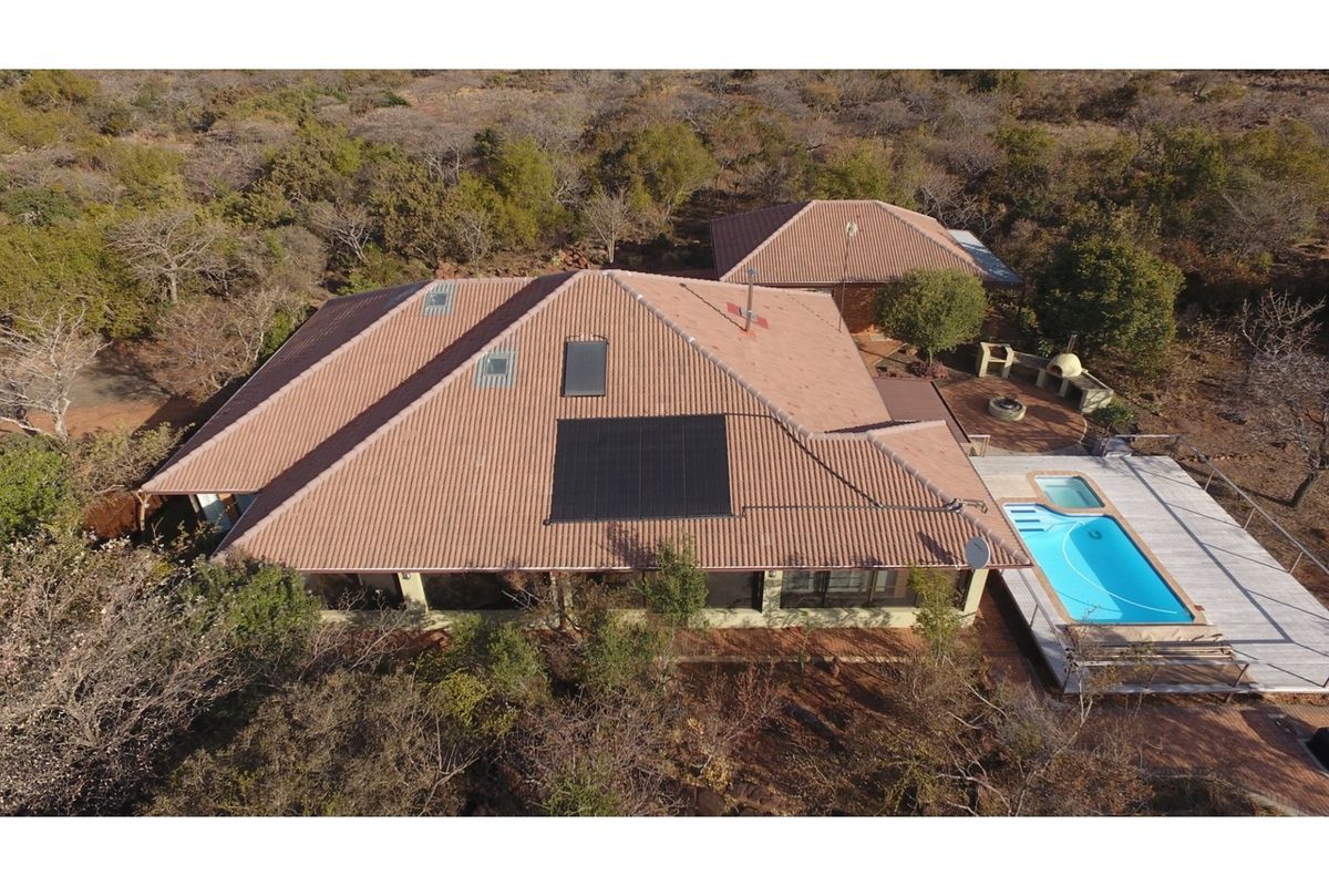Aerial view of the property featuring a tiled roof with solar panels, a swimming pool, and an outdoor entertainment area with a built-in braai.