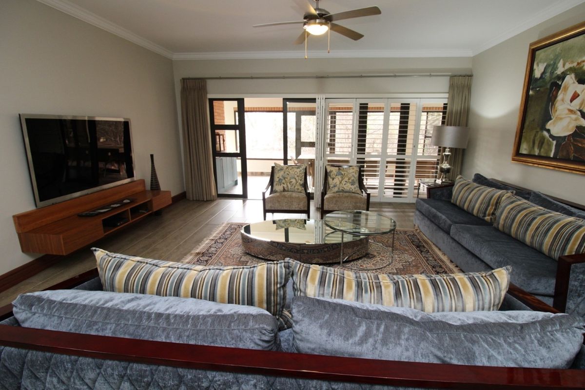 Spacious living room featuring tiled flooring, crown molding, a ceiling fan, and large sliding doors providing access to an outdoor patio area.