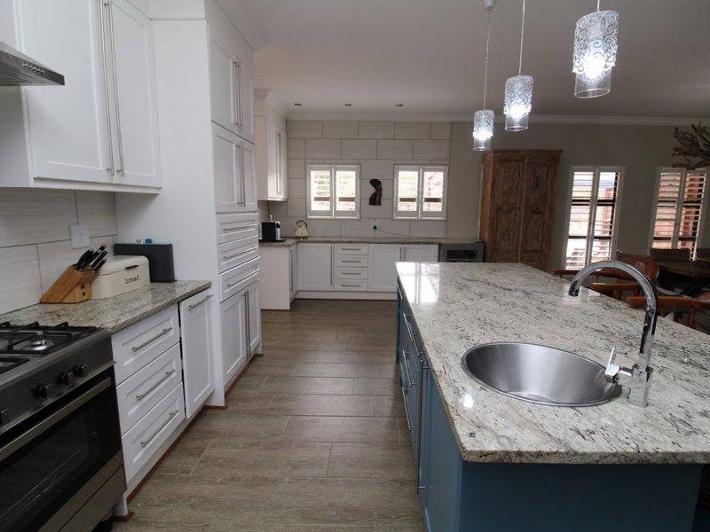 Spacious open-plan kitchen featuring a large granite-topped island with a prep sink, white cabinetry, and a stainless steel gas stove.
