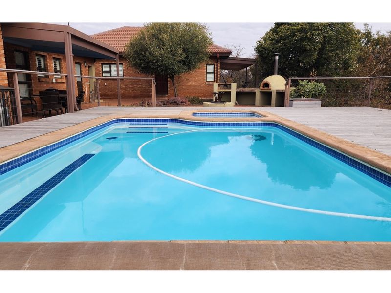 Outdoor pool area featuring a built-in pizza oven, wooden decking, and a covered patio area adjacent to the main brick residence.