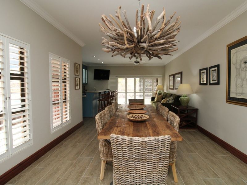 Spacious open-plan dining and living area featuring tiled flooring, plantation shutters, and a built-in bar counter with direct access to the patio.