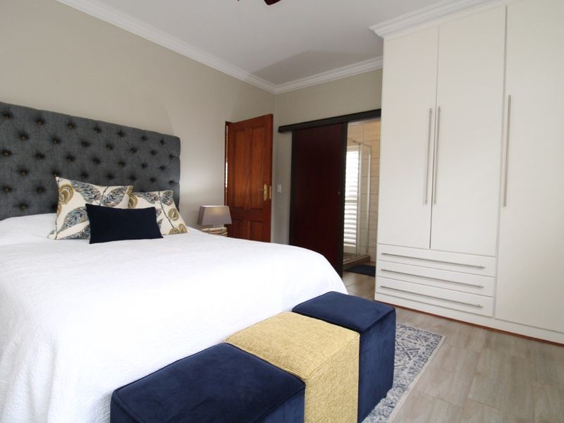 A well-maintained bedroom featuring built-in white cabinetry, crown molding, and an en-suite bathroom accessible via a sliding door.