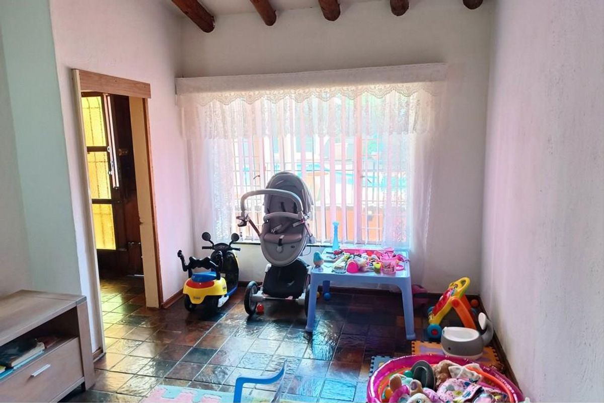 A versatile room featuring exposed timber ceiling beams and dark slate-style floor tiles, currently utilized as a play area with natural light.