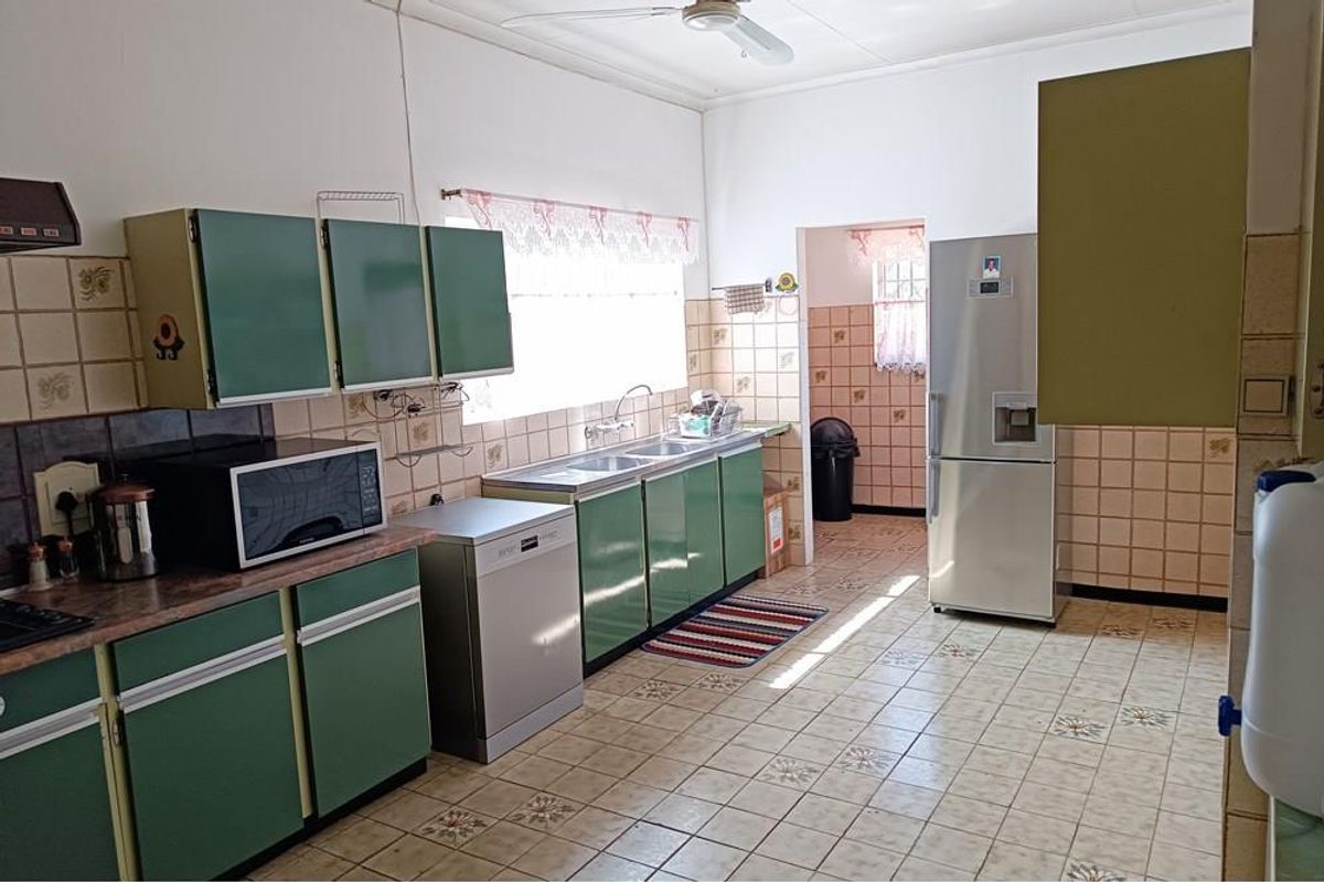 A dated kitchen featuring green cabinetry, tiled flooring, and a double sink, offering a functional layout with potential for modern renovation.