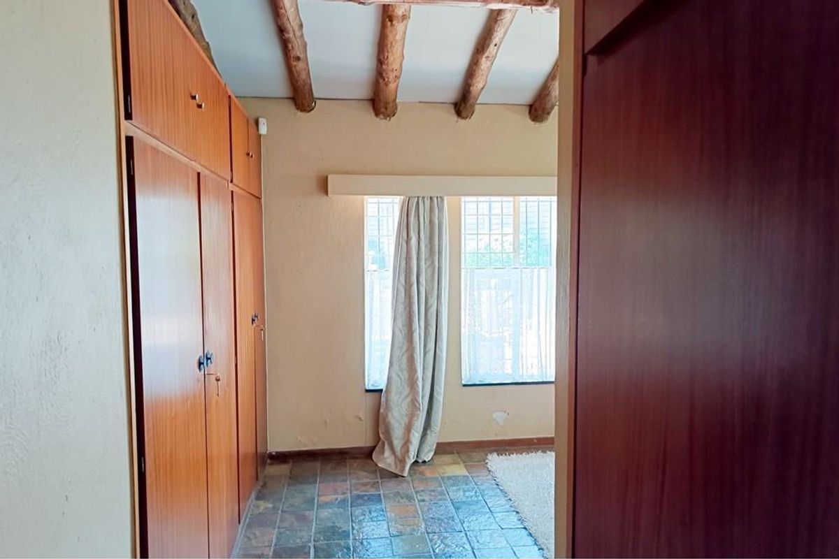 A bedroom featuring built-in wooden cabinetry, exposed timber ceiling beams, and tiled flooring, offering a rustic aesthetic with ample storage space.