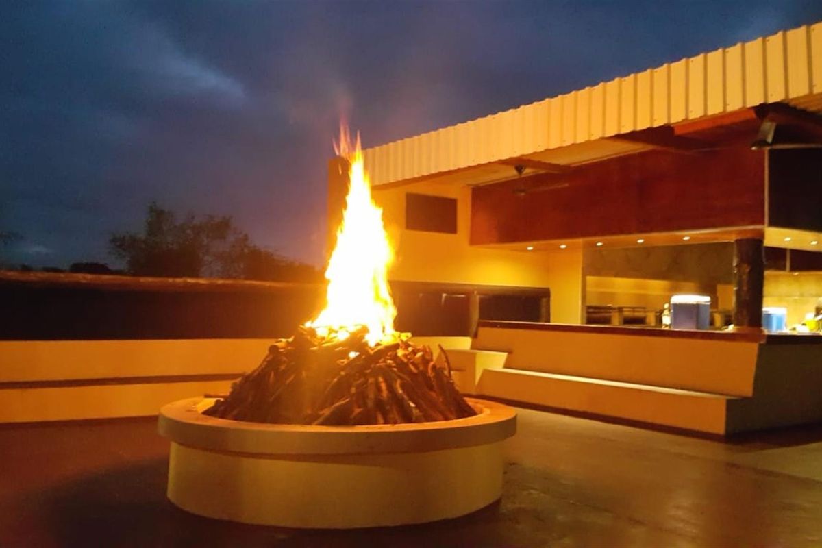 An inviting outdoor patio area featuring a large built-in fire pit and integrated bench seating under a covered roof, perfect for evening entertainment.
