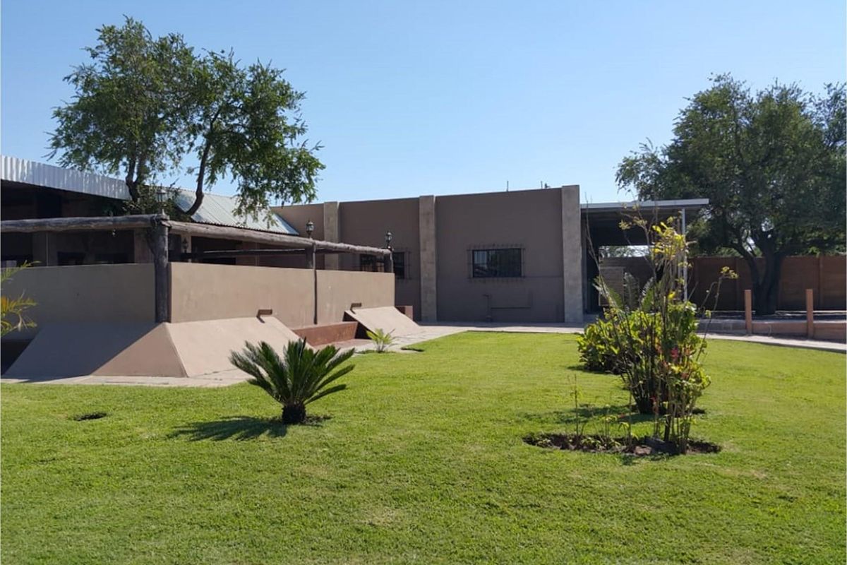 A view of the rear exterior of the farm property, featuring a well-maintained lawn, a covered patio area, and secure window fixtures.