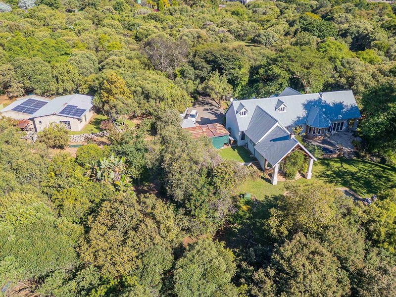 Aerial view of a small holding property featuring a main residence, a secondary outbuilding with solar panels, and extensive surrounding woodland.