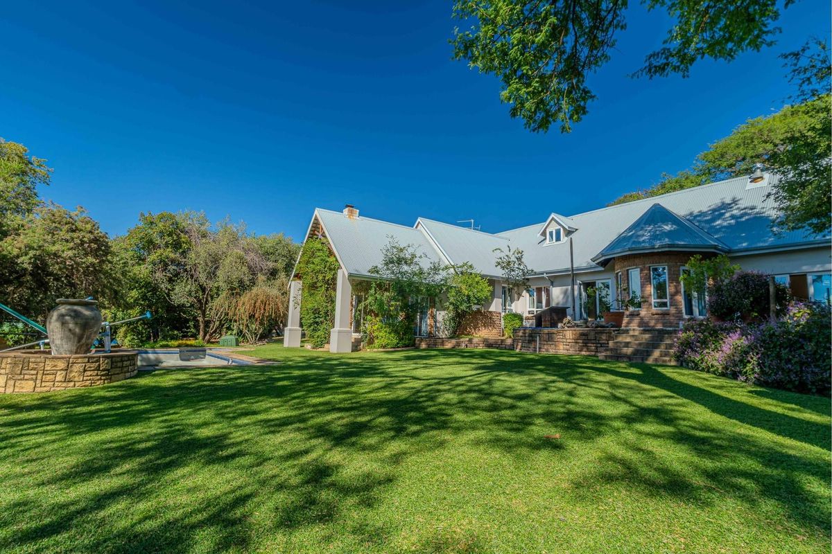 Spacious rear garden featuring a well-maintained lawn, established trees, and a swimming pool with a stone-clad water feature.