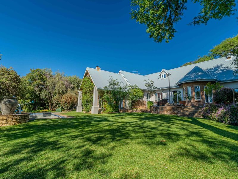 Spacious rear garden featuring a well-maintained lawn, established trees, and a swimming pool with a stone-clad water feature.