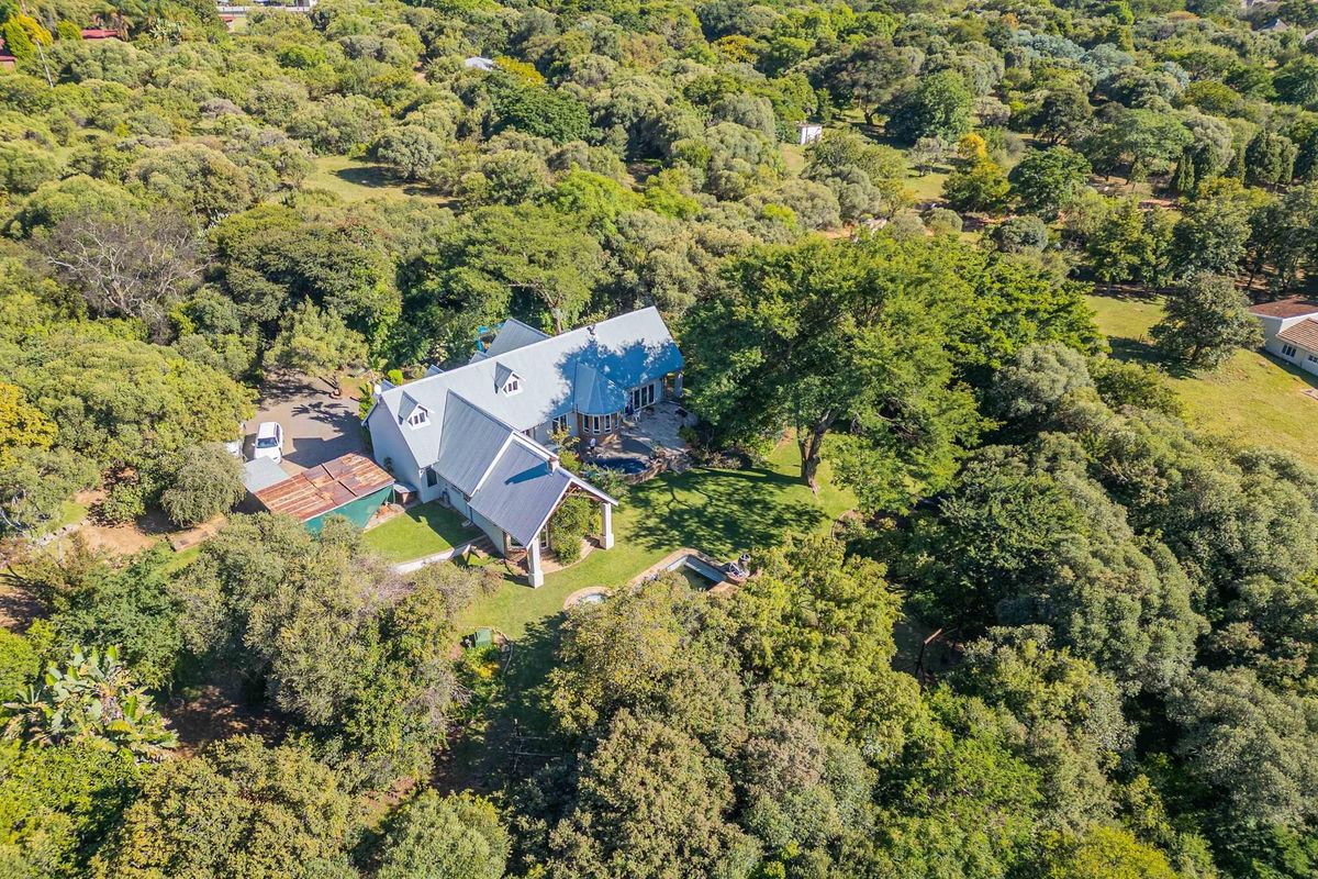 Aerial view of a spacious small holding property featuring a main residence with a metal roof, swimming pool, and extensive surrounding woodland.