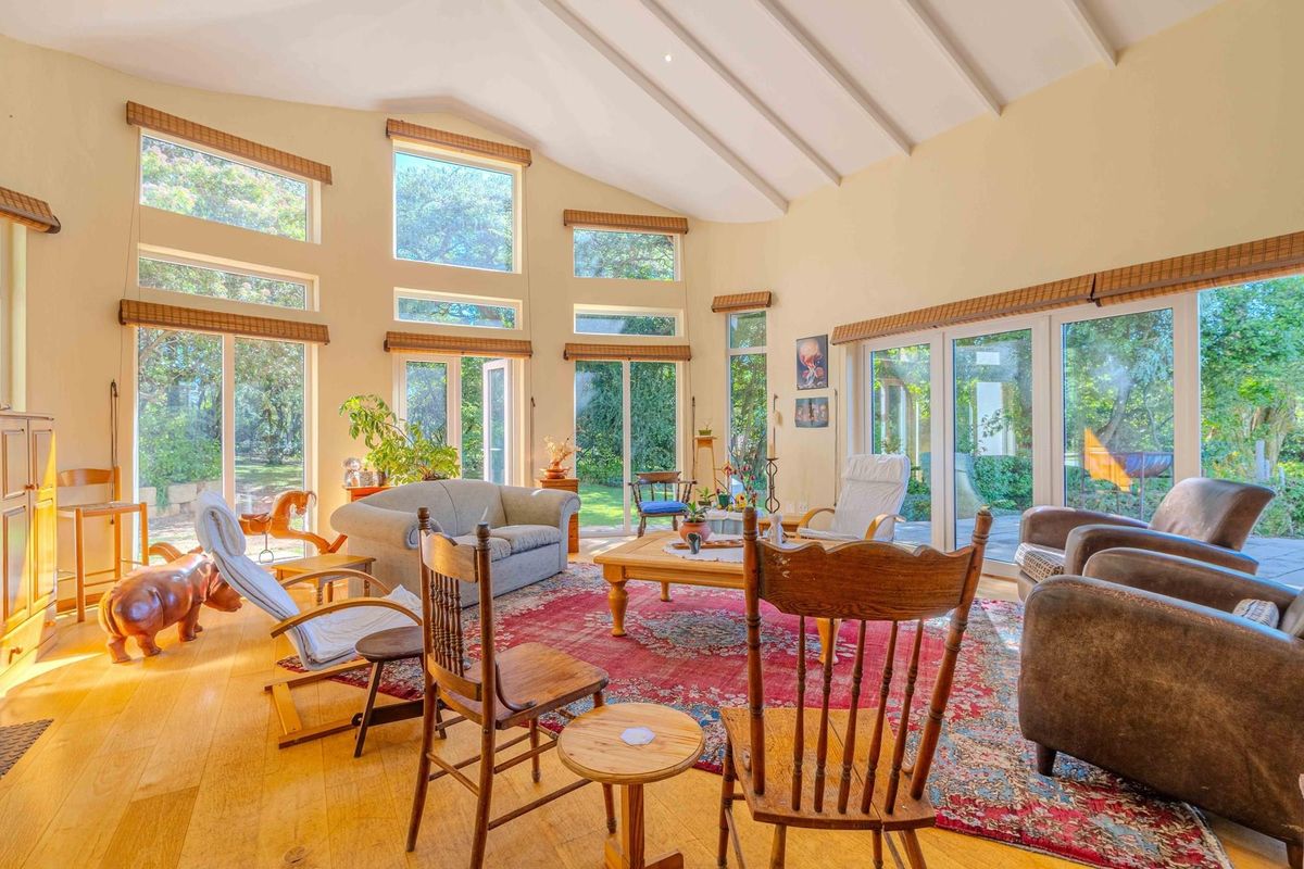 Spacious living room featuring vaulted ceilings with exposed beams, hardwood flooring, and extensive floor-to-ceiling windows providing abundant natural light and garden views.