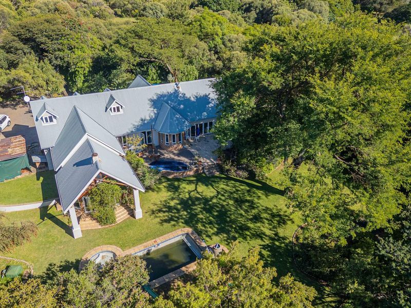 Aerial view of a small holding property featuring a large residence, expansive garden, swimming pool, and mature trees in a tranquil setting.
