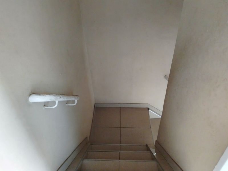 A narrow staircase featuring tiled steps and a wall-mounted handrail, showing signs of wear on the wall surfaces and handrail finish.