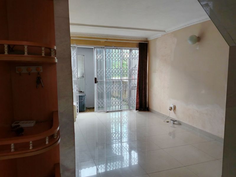 An empty living room featuring tiled flooring, a built-in shelving unit, and a sliding glass door with a security gate leading to the exterior.