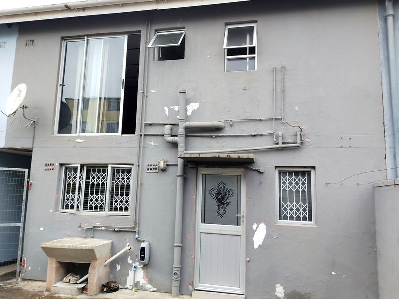 Rear exterior view of the property featuring a concrete wash basin, security gates on windows, and visible exterior plumbing and paint deterioration.