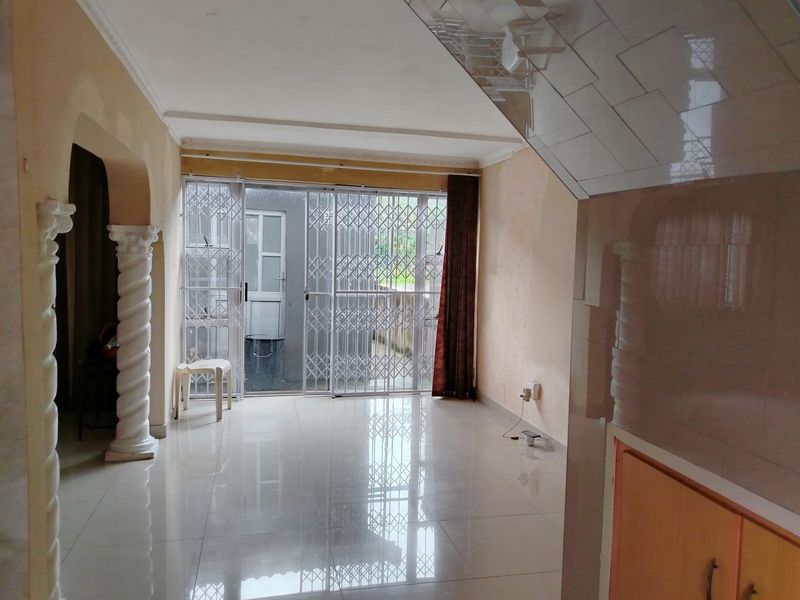 An empty living area featuring tiled floors, decorative columns, and a sliding glass door with a security gate leading to the exterior.