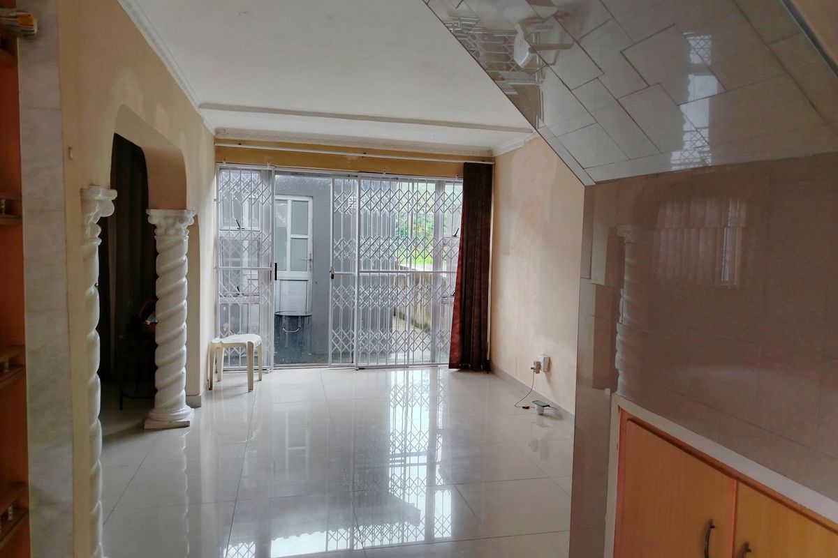 An empty living area featuring tiled floors, decorative columns, and a sliding glass door with a security gate leading to the exterior.