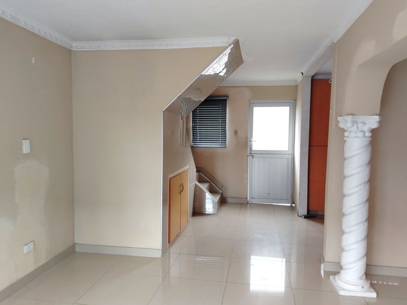 An empty living area featuring tiled floors, a decorative column, and built-in under-stair storage, requiring minor cosmetic wall repairs.