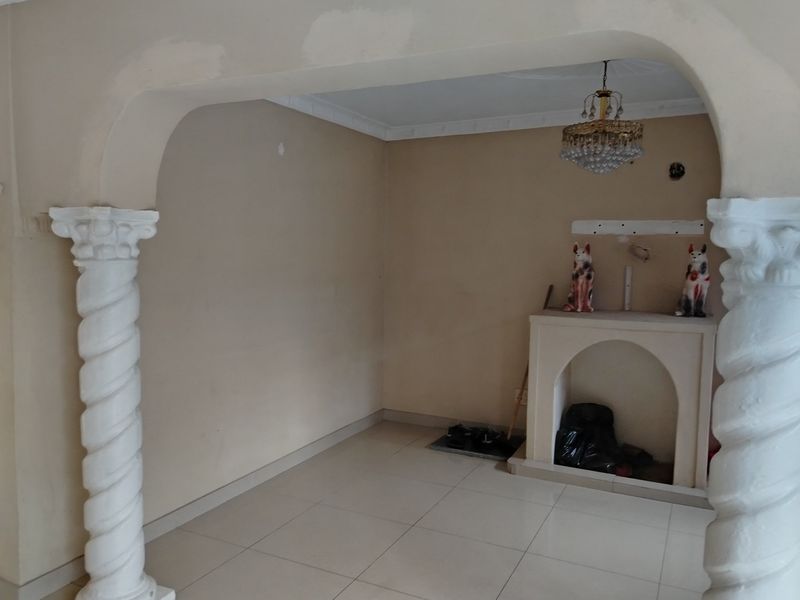 An empty living room area featuring decorative columns, an arched entryway, tiled flooring, and a built-in fireplace, requiring some cosmetic wall repairs.