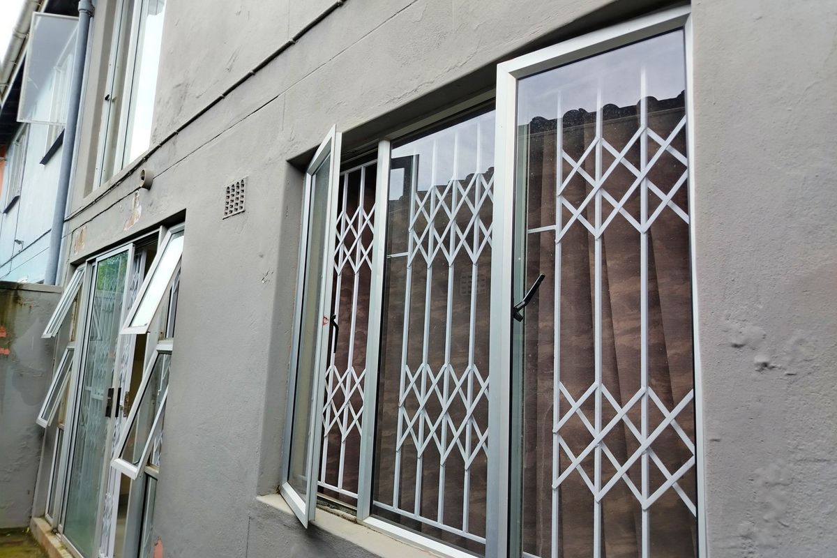 Exterior view of the rear wall featuring aluminium window frames with fitted security gates and a ventilation brick.
