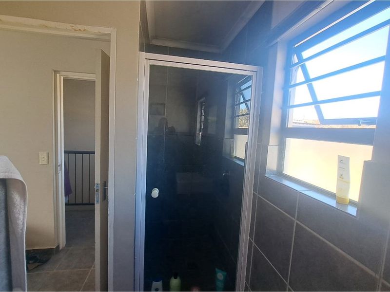 A functional bathroom featuring a glass-enclosed shower, tiled walls, and a window with louvre shutters, providing natural light and ventilation.