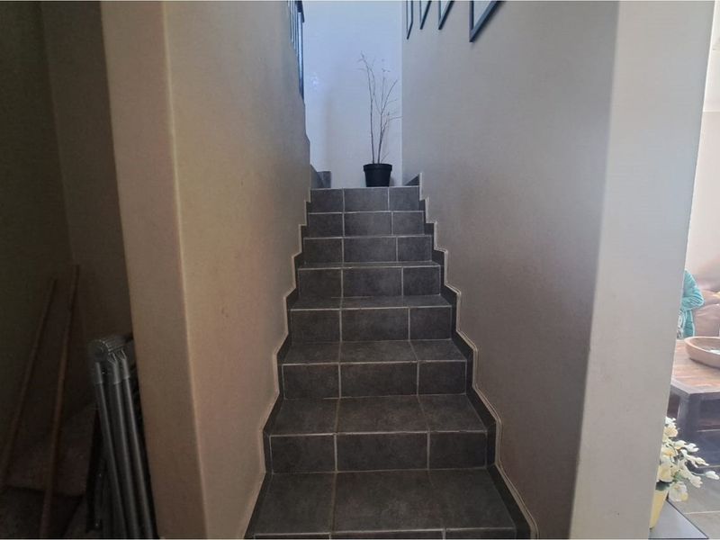 A staircase featuring dark ceramic floor tiles, leading upwards between two neutral-toned walls.