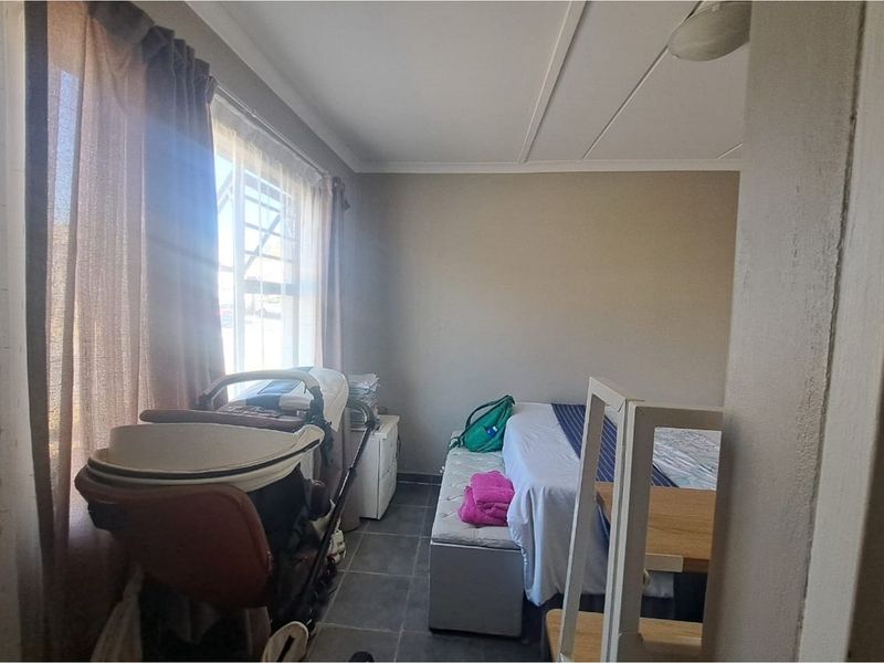A bedroom featuring tiled flooring and a large window allowing natural light, providing a functional space for rest.