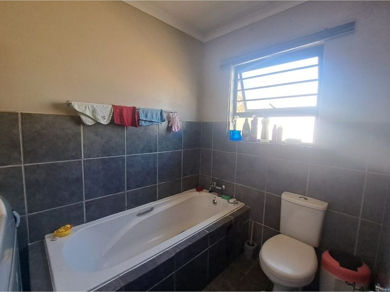 A functional bathroom featuring a built-in bathtub, tiled walls, and a standard toilet with a window for natural ventilation.