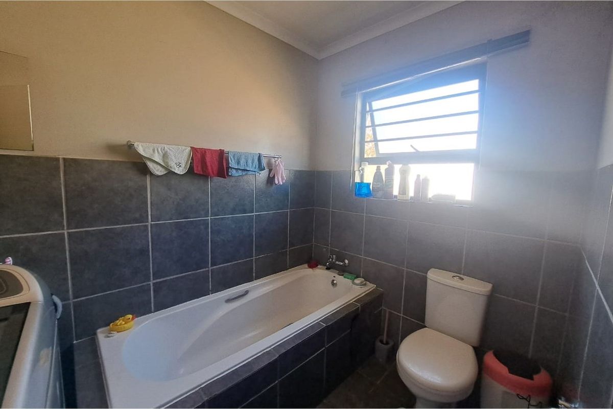 A functional bathroom featuring a built-in bathtub, tiled walls, and a standard toilet with a window for natural ventilation.