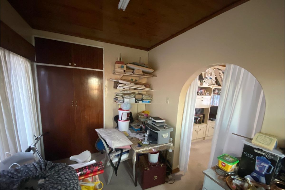 A bedroom featuring built-in timber cabinetry and a wood-paneled ceiling, connected to an adjacent living space via an arched doorway.