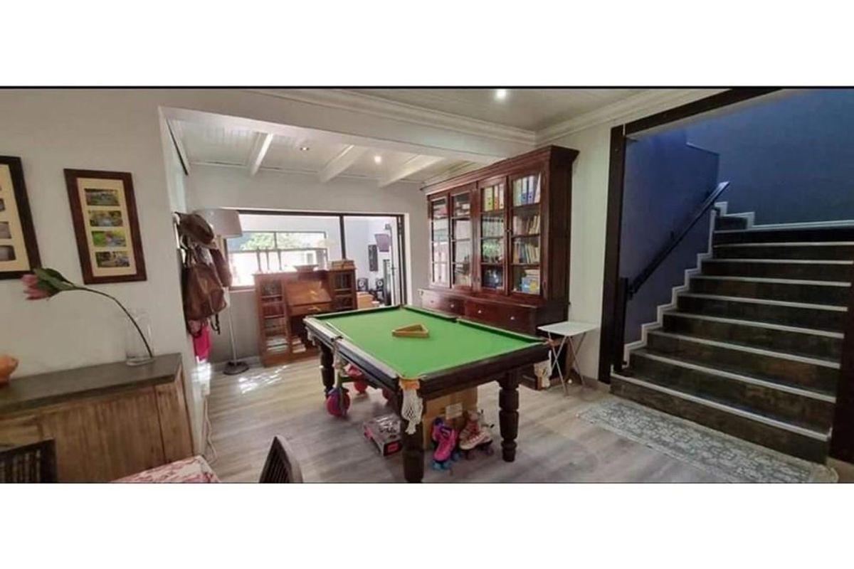 A multi-purpose living area featuring a staircase with a dark handrail, exposed beam ceiling details, and wood-look flooring.