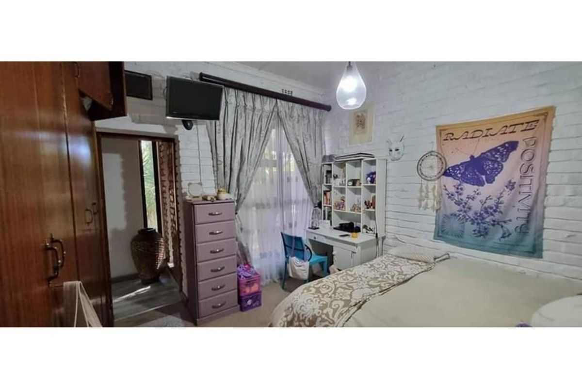 A bedroom featuring painted brick walls, built-in wooden cabinetry, and a window with curtain treatments.