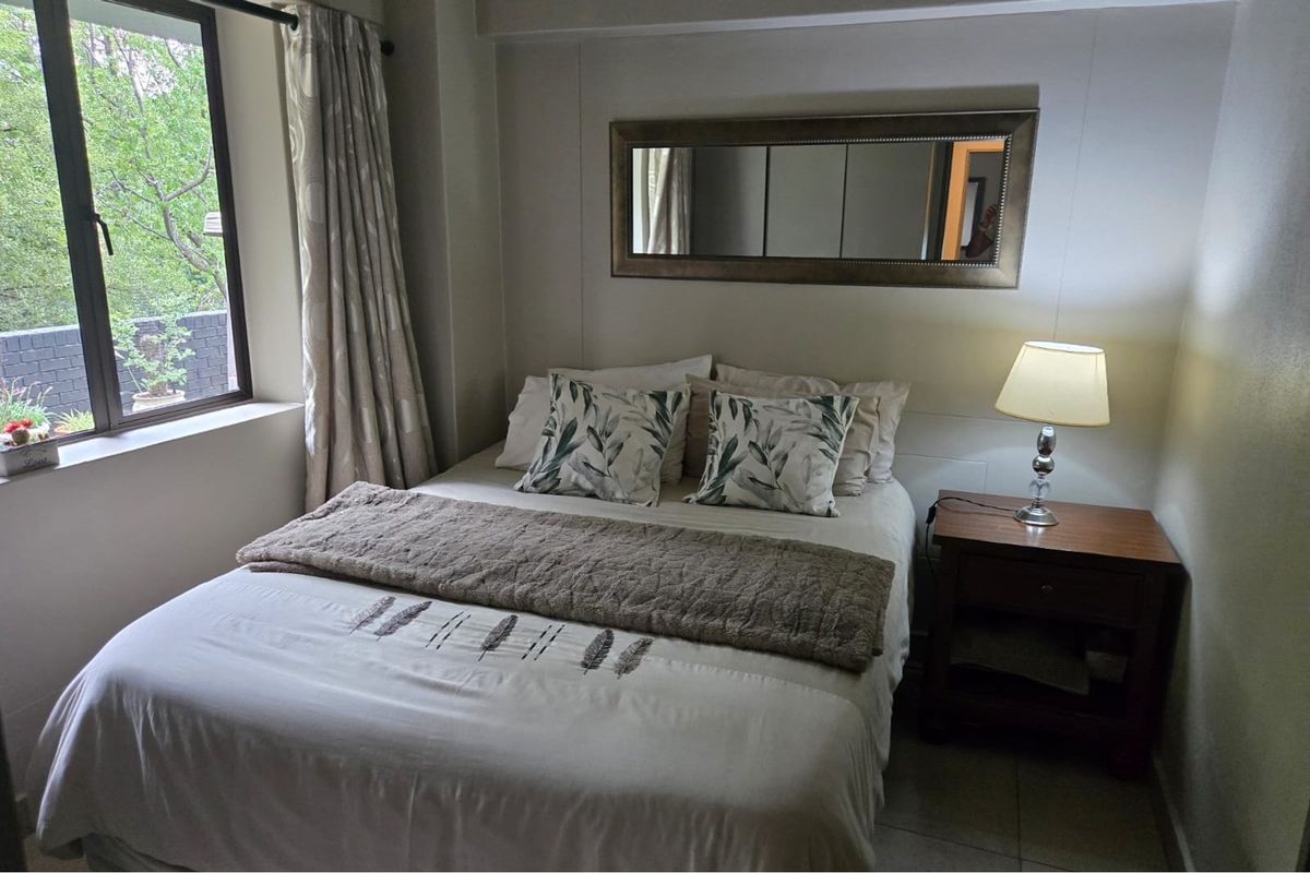 A cozy bedroom featuring a large window with natural light, tiled flooring, and neutral wall finishes.